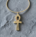 Gold ankh pendant on a textured gray background
