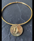 Gold bracelet with a round, textured disc on a dark surface