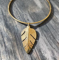 Gold necklace with a leaf-shaped pendant on a wooden surface