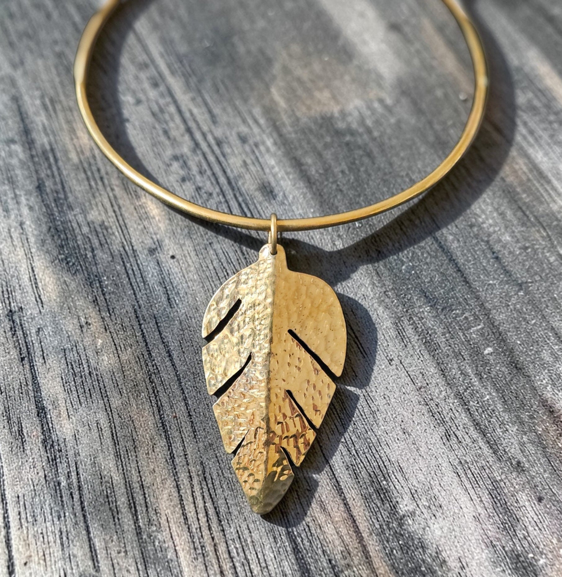 Gold necklace with a leaf-shaped pendant on a wooden surface