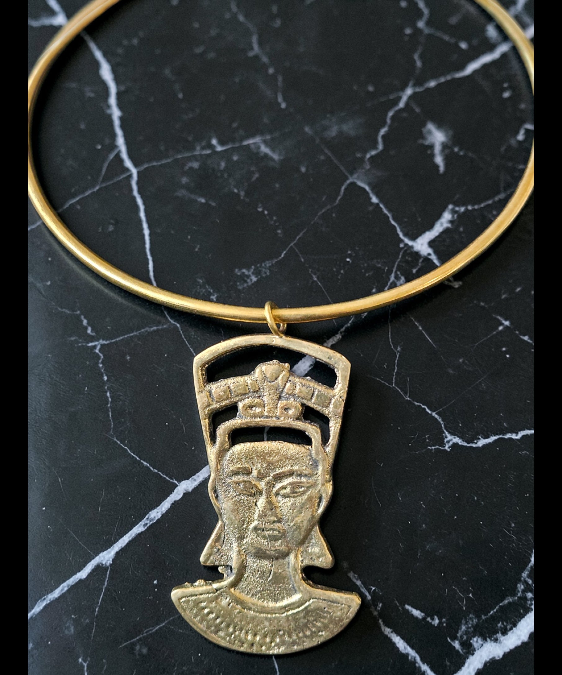 Gold necklace with a pendant of a face on a black marble surface